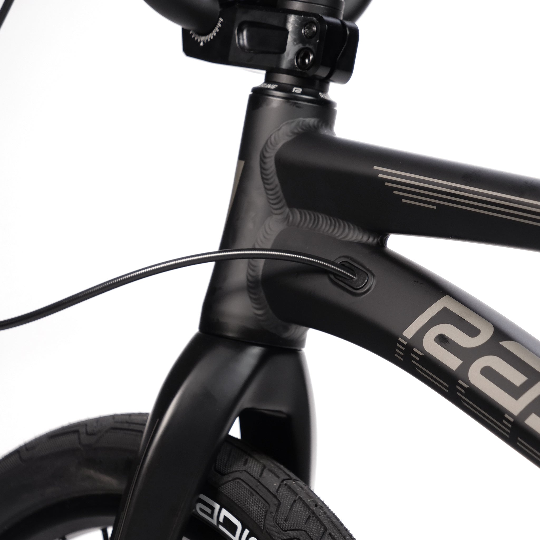 Close-up of a Radio Quartz Pro XL Bike 2025 frame's front section, showcasing the junction between the head tube and downtube, with a cable routed elegantly through the lightweight hydro-formed structure and part of the front tire in view.