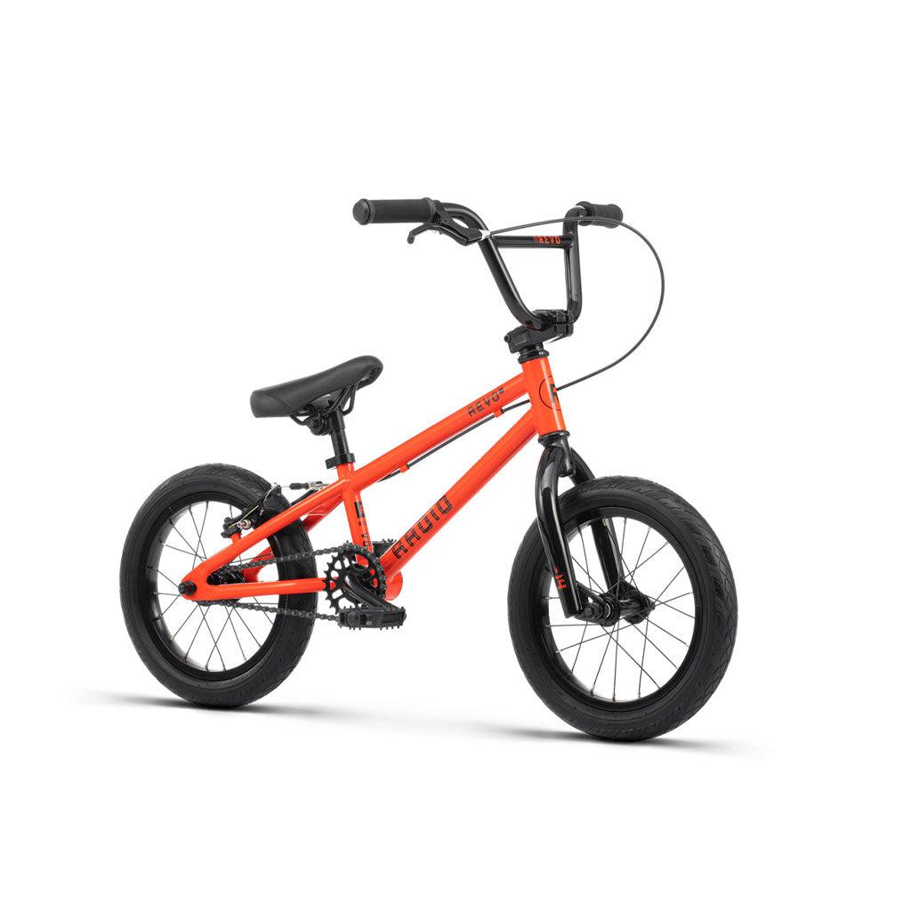 A small orange Radio Revo 14 Inch bike with black handlebars, black seat, and thick black wheels. The frame features the brand name, "REDLINE," making it an ideal first bike for young enthusiasts.