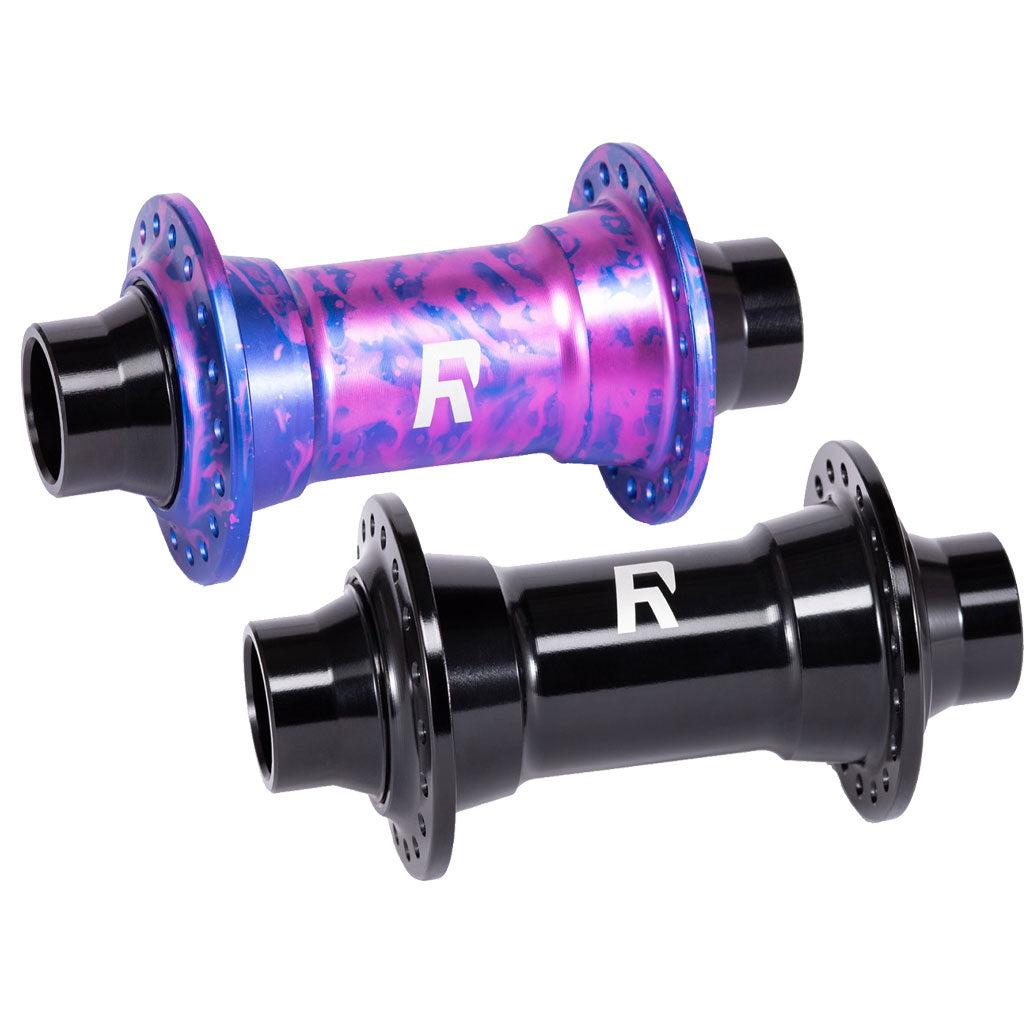 Two bicycle hubs are shown: one is colorful with a mix of blue and pink hues, and the other is solid black. Both display a white logo. The vibrant hub, crafted from 6061-T6 alloy, adds flair to street riding or slopestyle adventures, while the solid black Radio Sonar Front Hub (32 Hole) is perfect for your MTB front end.