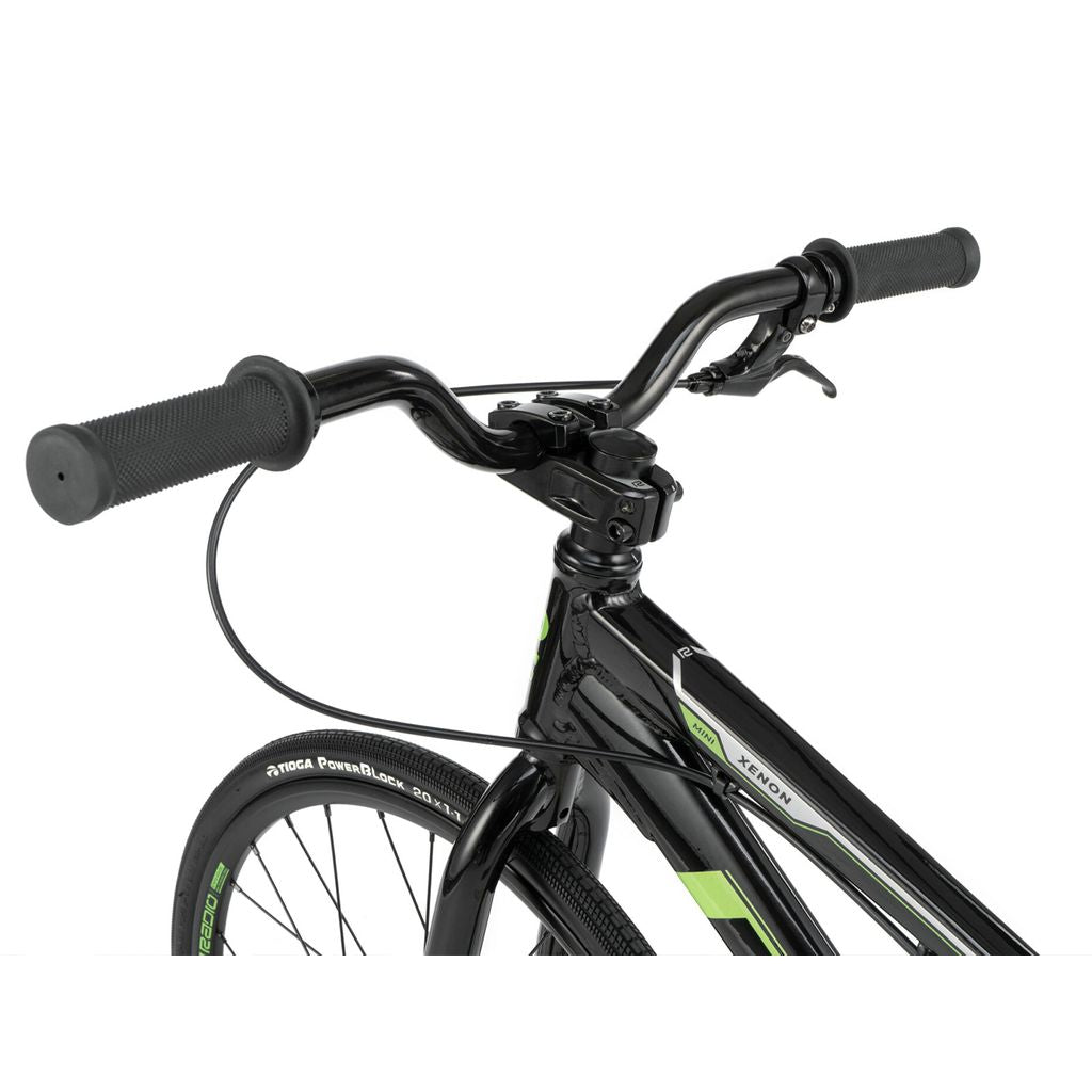 Close-up of black handlebars with textured grips and attached brake levers on a Radio Xenon Mini Bike; partial view of the black hydro-formed 6061-T6 alloy frame and front wheel with thin tires.