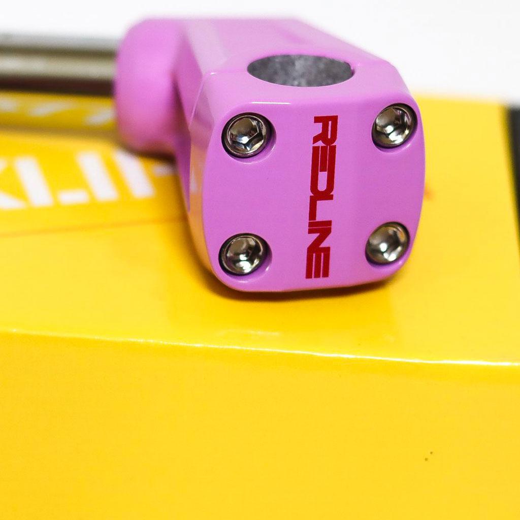 A close-up of a pink REDLINE BY KASTAN Forklifter Front Load Stem, featuring bold red "Redline" text, sits on a vibrant yellow box. Four screws adorn the stem's face, showcasing BMX Freestyle craftsmanship.