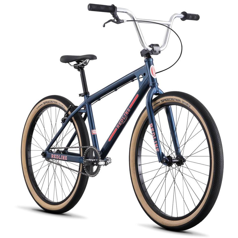 A Redline SQB 26 Inch Bike, featuring a blue frame with tan tires and black handlebars that highlight its BMX heritage and sleek design, is displayed from the side against a white background.