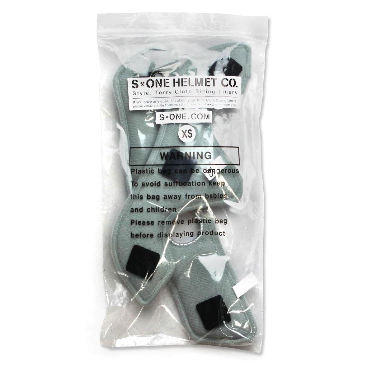 A clear plastic bag containing XS-sized S-One Helmet Wide Terry Cloth Liners, designed as washable sweat-absorbing replacements for helmet sizing. The bag has warning labels to keep out of reach of babies and children due to potential suffocation hazards.