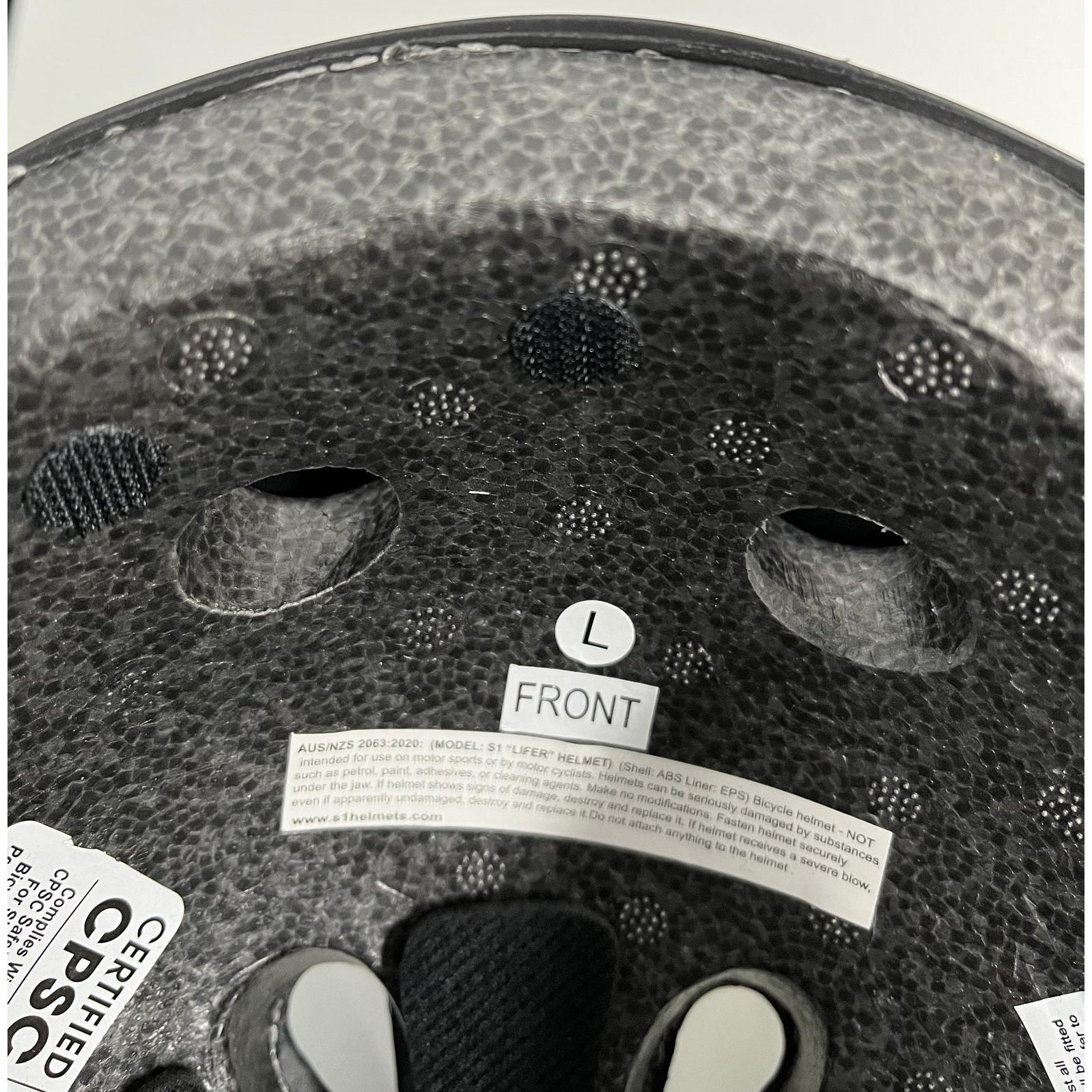 The inside of a bicycle helmet displaying texture, ventilation holes, label 'FRONT', size 'L', and safety certification stickers, equipped with a handy S-One Lifer (12 Pack) Velcro Kit Round Dots for easy adjustments.