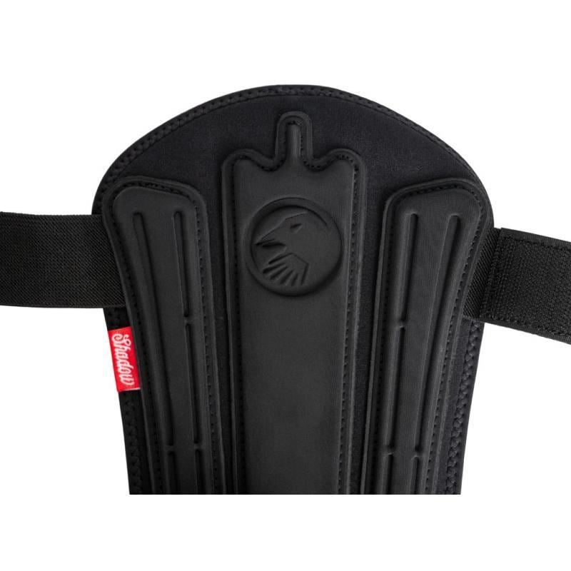 Close-up of black protective padding with vertical ridges and a circular lion head emblem. Crafted with 3D impact foam for superior defense, this is the Shadow Invisa-Lite Shin/Ankle Pad Combo (Youth). A red tag reads "Sfamay.
