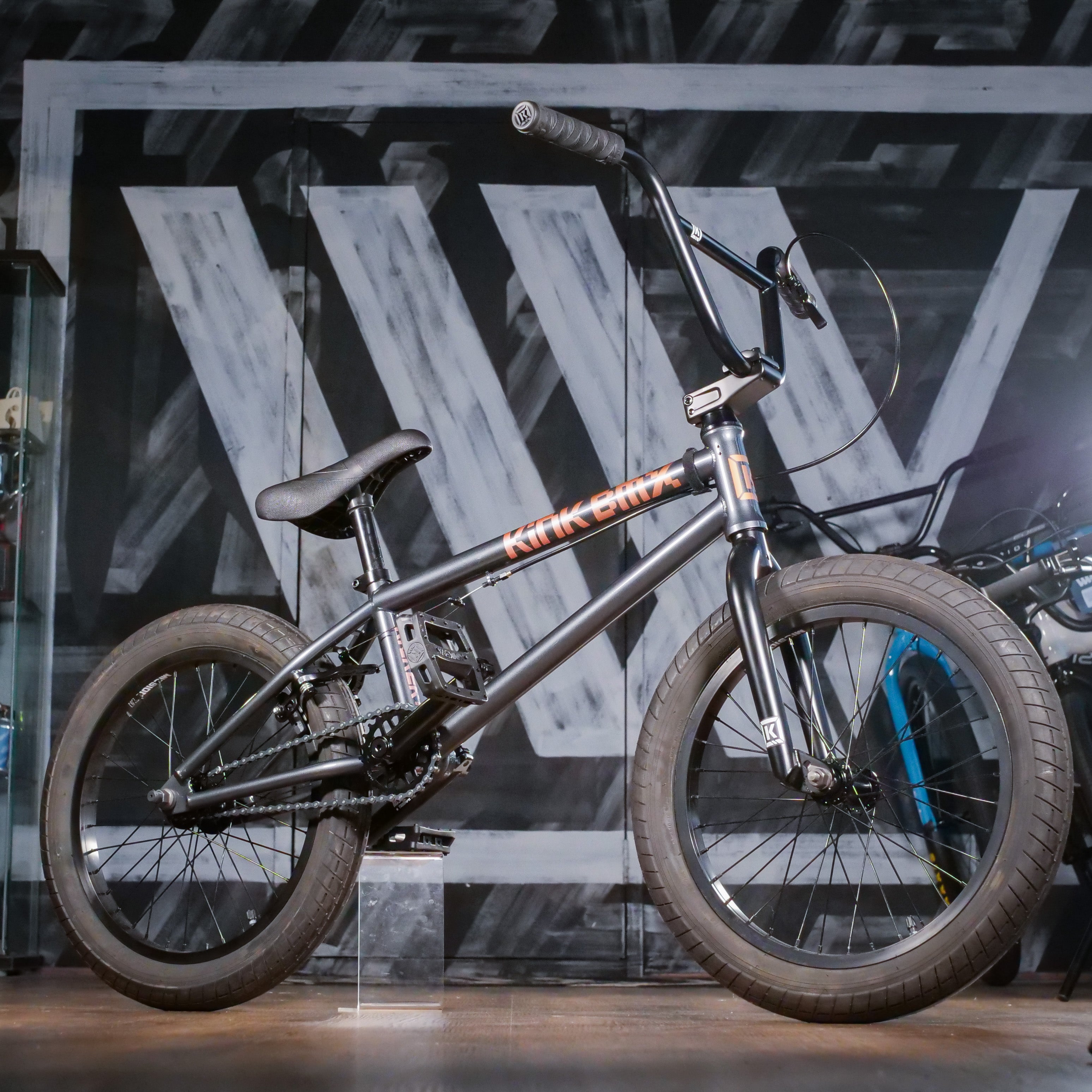 The Kink Kicker 18 Inch Bike (2026), featuring thick tires, is displayed indoors against a graffiti-style wall with bold white and gray lettering.