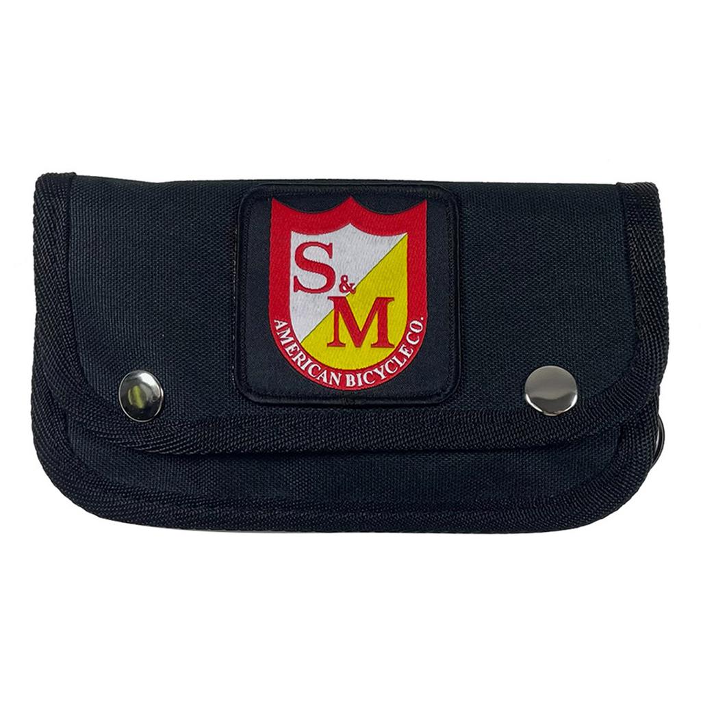 The S&M Trucker Wallet is a black pouch with snap buttons, a snap belt loop, and features a red and yellow "S&M American Bicycle Co." logo patch, offering style and security for your essentials.