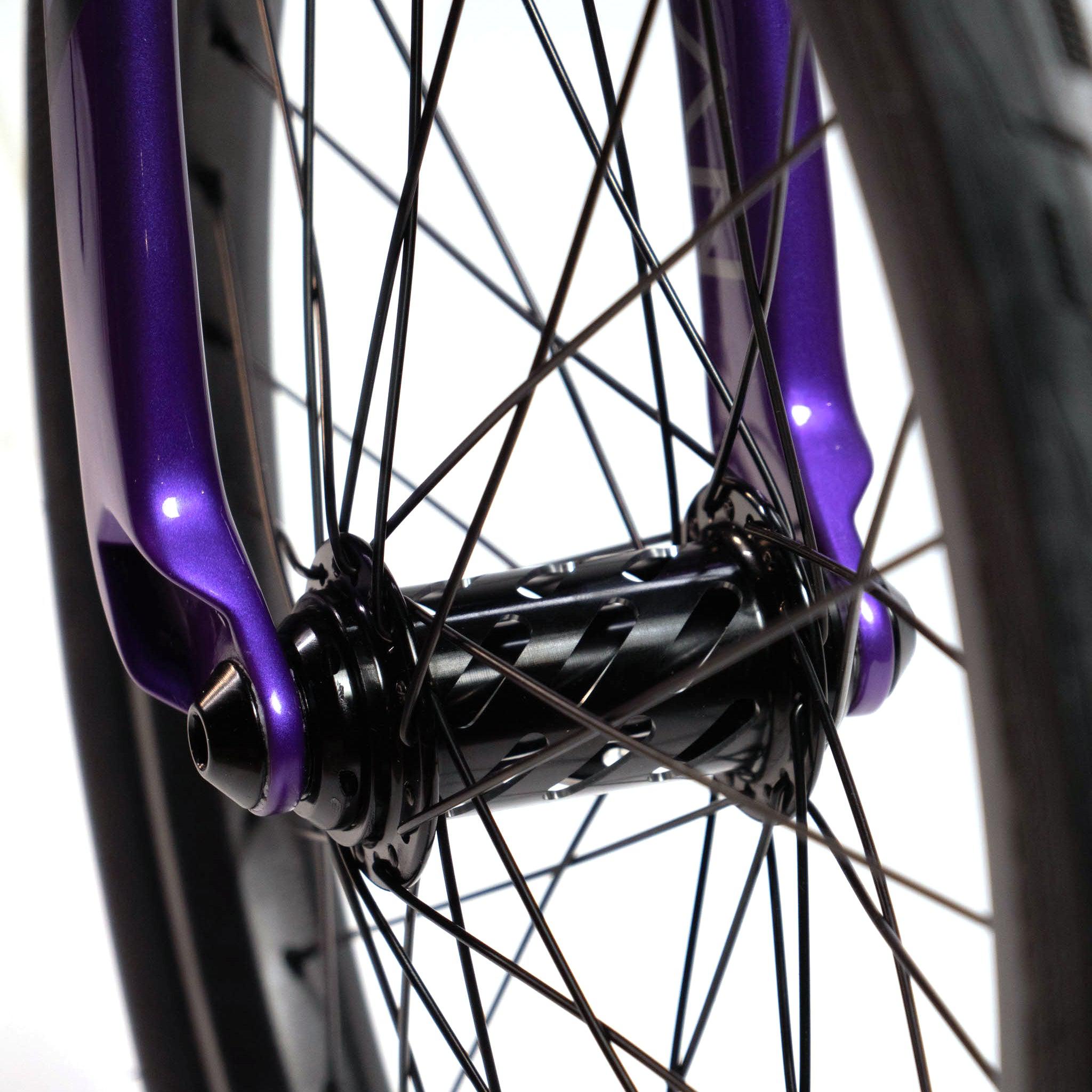 Close-up of the Speedco Velox Evo Pro XXXL Custom Bike's front wheel and fork, highlighting the purple fork legs, black spokes, and a black hub adorned with a patterned design.