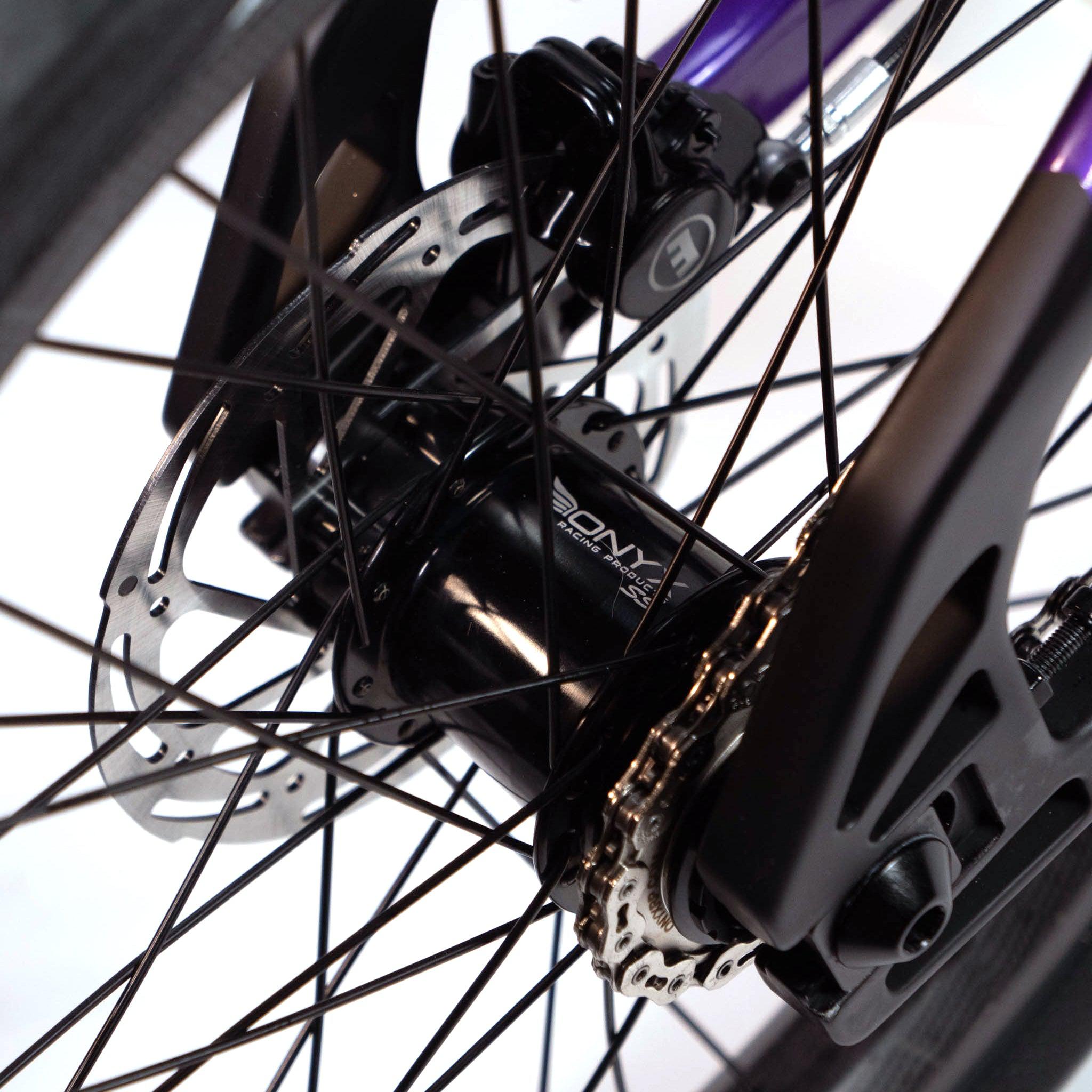 Close-up of a Speedco Velox Evo Pro XXXL Custom Bike wheel assembly showcasing the hub, disc brake rotor, and spokes, with a partial view of the custom race bike frame in the background.