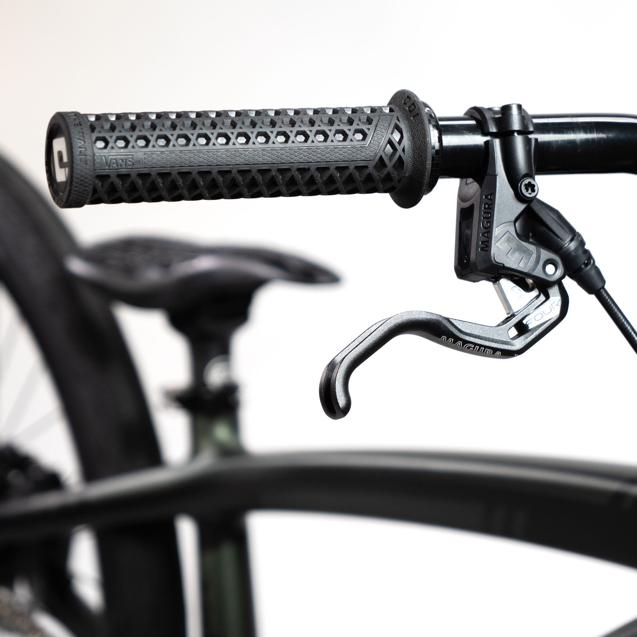 Close-up of the Speedco Velox Pro XL Cruiser Custom Bike handlebar showcasing a textured grip and branded brake lever, with the seat and tire subtly blurred in the background.