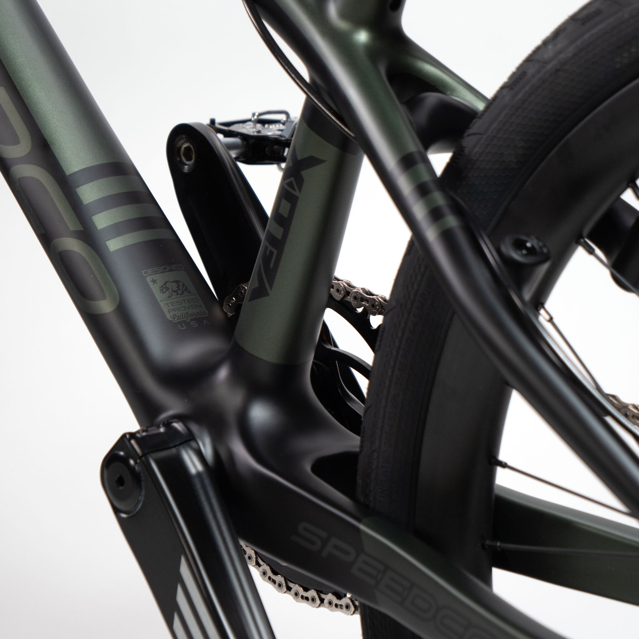 Close-up of the matte black and green frame of a cruiser bike, highlighting the chain and suspension system details with the text "Vora" and "Speedco Velox Pro XL Cruiser Custom Bike.
