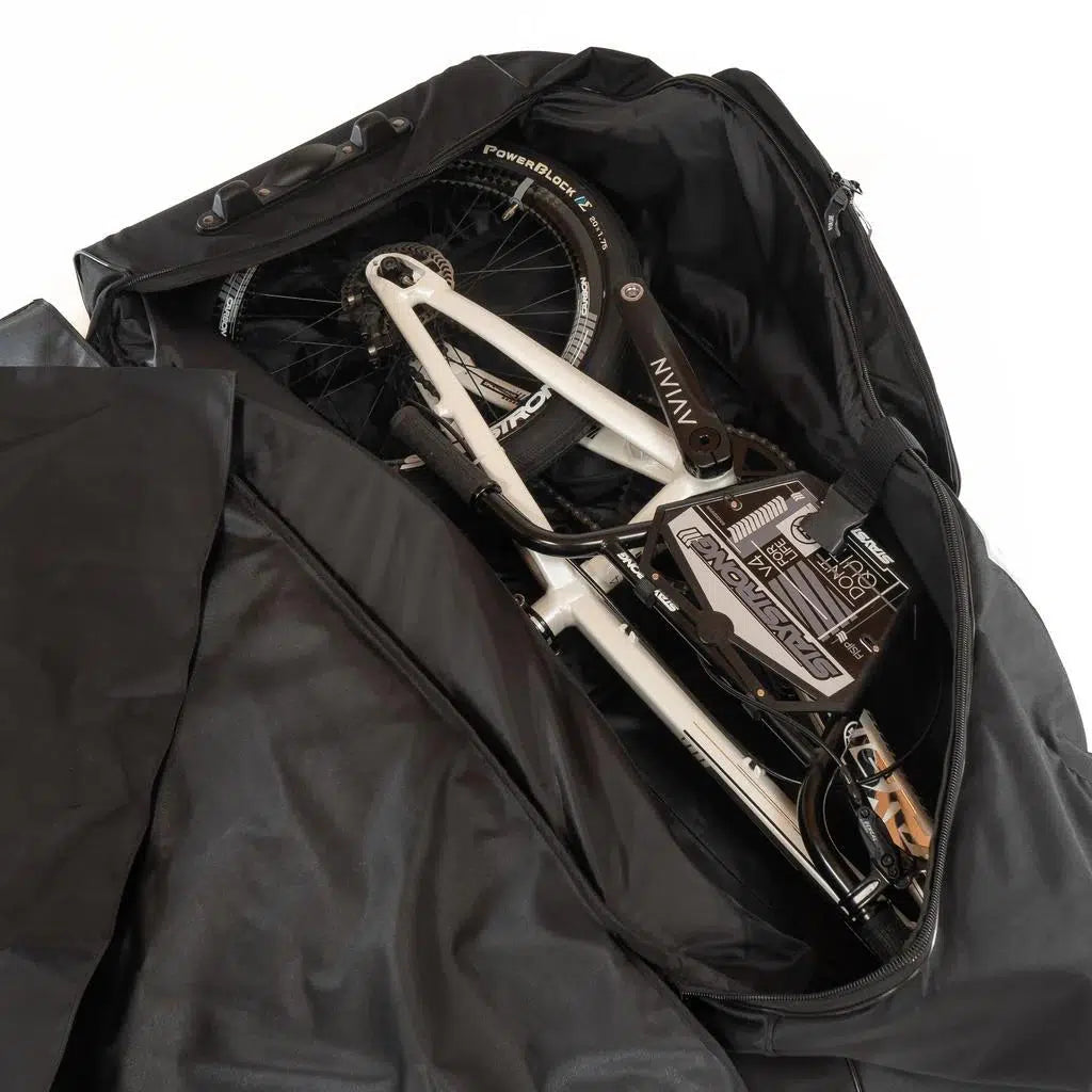A bicycle is disassembled and packed inside a partially unzipped Stay Strong Bike Carry Bag V2, revealing the bike components and frame.