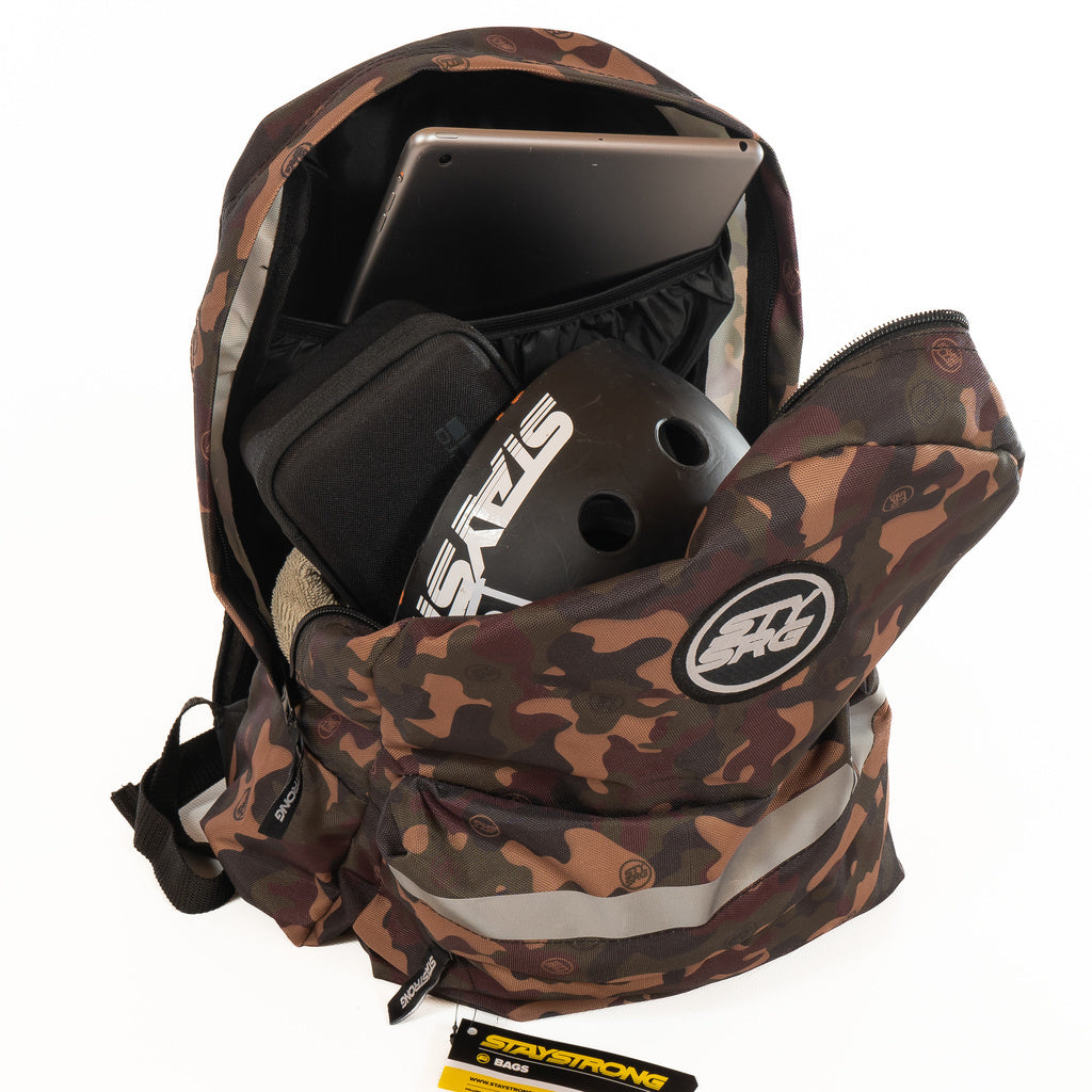 A Staystrong Backpack Chevron V3 with adjustable shoulder straps is open, revealing a laptop in its dedicated sleeve, a black “STAY STRONG” helmet, a pair of shoes, and a black pouch inside.