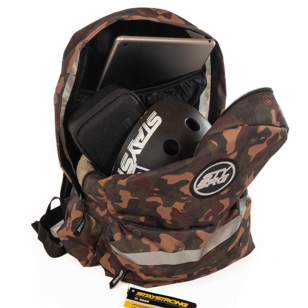 A Staystrong Backpack Chevron V3 with adjustable shoulder straps is open, revealing a laptop in its dedicated sleeve, a black “STAY STRONG” helmet, a pair of shoes, and a black pouch inside.