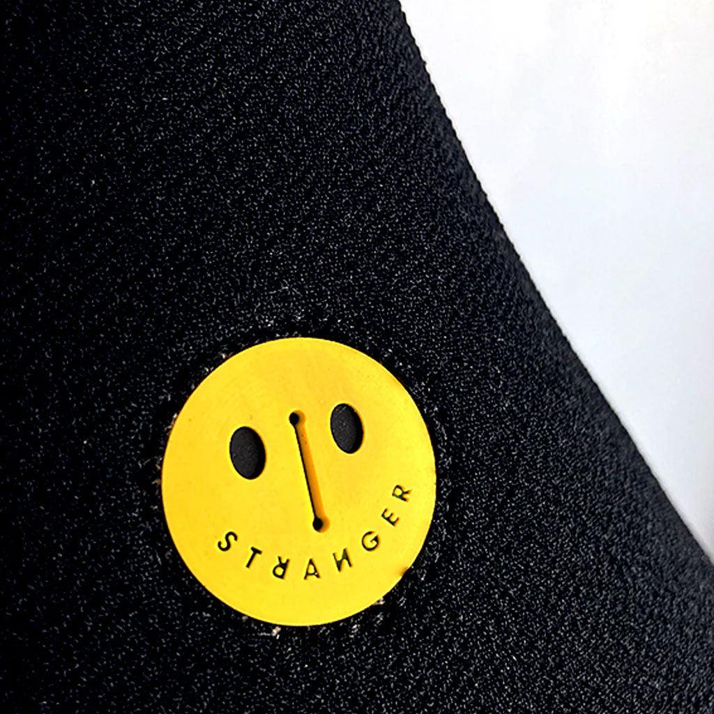 A black fabric features a custom-molded patch with a small yellow circular design of a smiling face and the word "Stranger JCAP Pivotal" in black text.