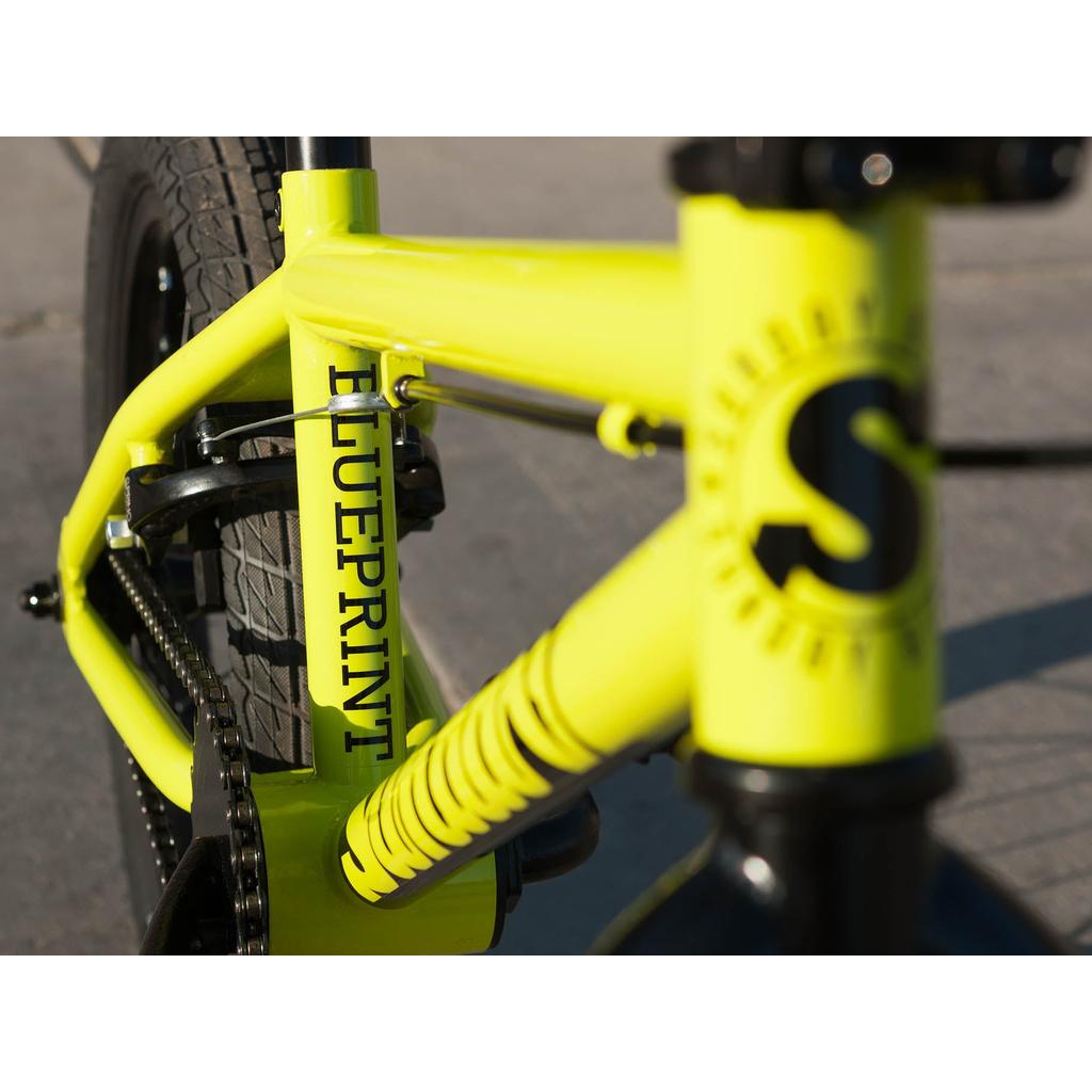 Close-up of a yellow Sunday Blueprint 16 Inch Bike frame with scaled-down geometry, "BLUEPRINT" printed on it, and part of the front wheel and fork visible.
