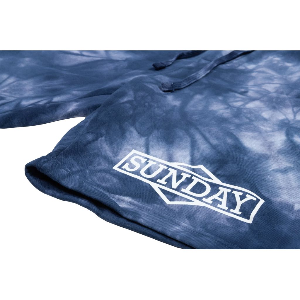 Close-up of blue tie-dye fabric with a white "SUNDAY" logo printed on it, showcasing the intricate pattern and vibrant hues of the Sunday Cornerstone Sweat Shorts. For the perfect fit, refer to our Size Guide for inseam and waist inches.