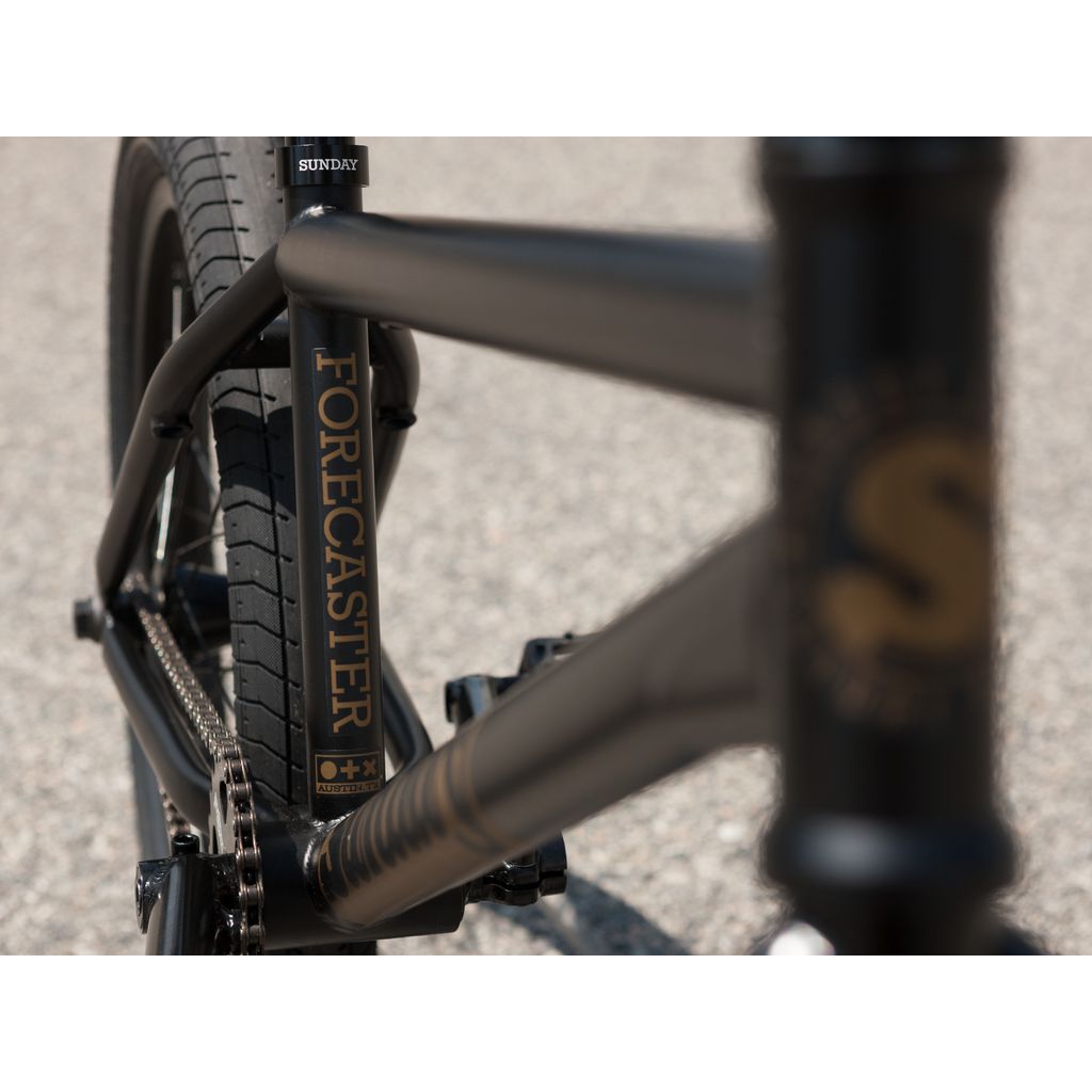 Close-up of the Sunday Forecaster Broc Raiford 20 Inch Bike (2023) in black, showcasing the chain, rear wheel, and chromoly frame with the brand name “Sunday” clearly visible.