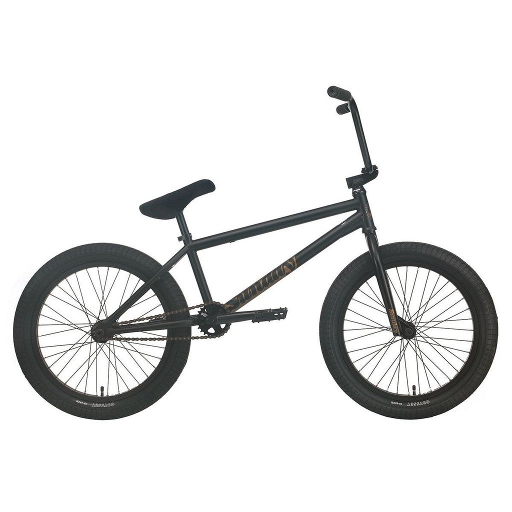 Side view of a matte black, Sunday Forecaster Broc Raiford 20 Inch Bike (2023) against a corrugated metal backdrop. Text lists features including a 100% chromoly frame, Odyssey clutch V2 freecoaster, and aftermarket parts.