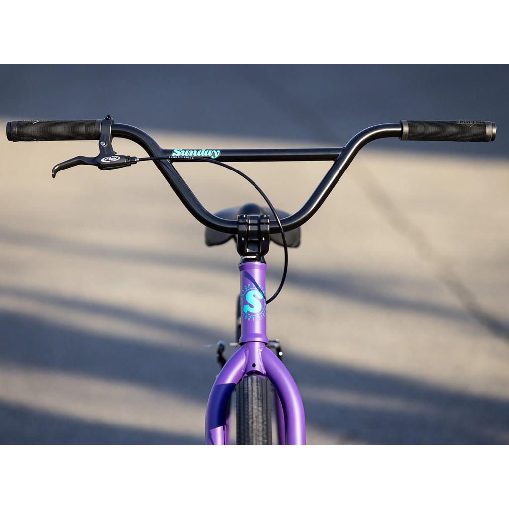 Front view of the Sunday High C 29 Inch Bike (2025) with a purple chromoly frame, black handlebars, and visible brake lever, photographed outdoors on pavement.
