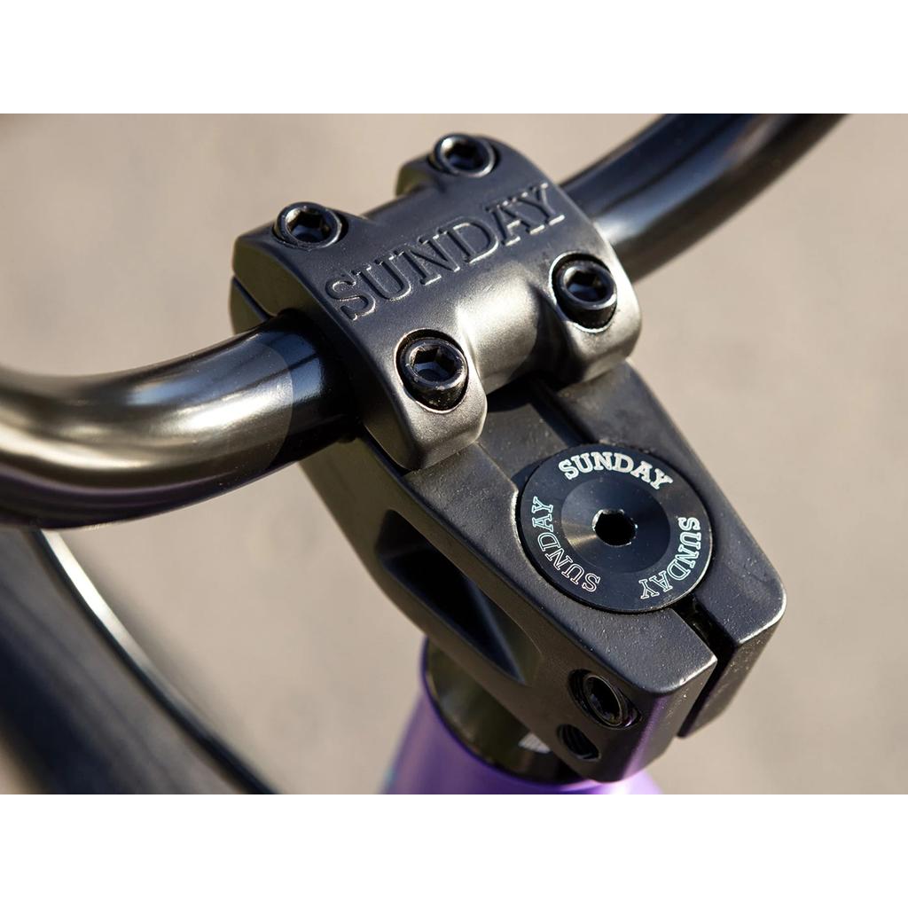 Close-up of the Sunday High C 29 Inch Bike (2025) showing black BMX stem and handlebars with "SUNDAY" branding, a sturdy chromoly frame, and a blurred background.