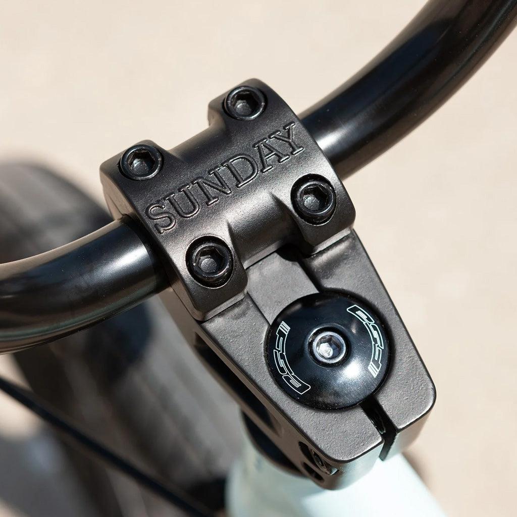 Close-up of the Sunday Primer 20 Inch Bike's handlebars showing the top clamp branded with "SUNDAY" and a black round component, highlighting its pro-level geometry.