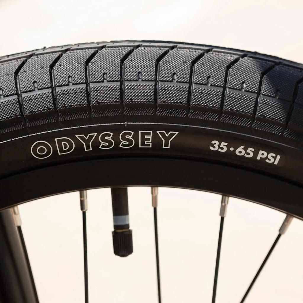 Close-up of a bicycle tire with the brand name "Odyssey" and pressure range "35-65 PSI" visible on the sidewall, showcasing textured tread and several wheel spokes—perfect for riders of the Sunday Primer 20 Inch Bike.