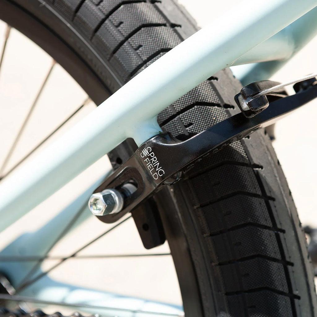 Close-up of a Sunday Primer 20 Inch Bike’s rear wheel, highlighting the tire, frame, and a brake component labeled "Springfield," showcasing its starter bike appeal with pro-level geometry.
