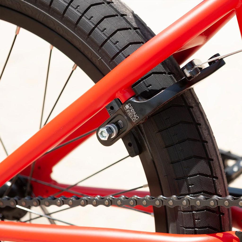 Close-up of the rear wheel of a red Sunday Primer 20 Inch Bike showcasing the tire, rim, spokes, and brake system, along with part of the chain and frame – an excellent starter bike featuring pro-level geometry.