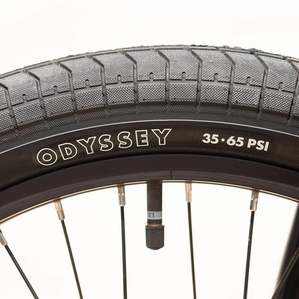 Close-up of a bicycle tire with the word "Odyssey" printed on it, featuring a pressure range of 35 to 65 PSI on the sidewall. The tire is mounted on a black wheel rim with metal spokes, reminiscent of the pro-level geometry seen in high-quality models like the Sunday Primer 20 Inch Bike.