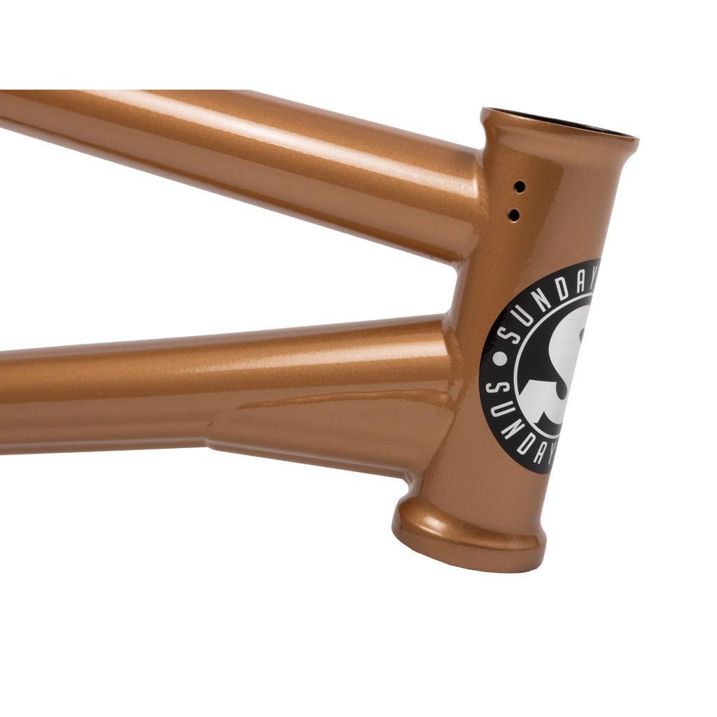 Close-up of the metallic bronze Sunday Silvawave Frame (Brett Silva Signature) featuring a black and white "Sunday" logo sticker on the head tube, showcasing its premium chromoly construction.