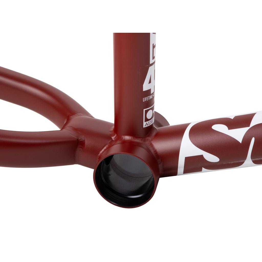 Close-up of a red Sunday Soundwave V3 Frame's 4130 Chromoly bottom bracket area, showing welds, part of the chainstays and downtube, and white lettering on the frame.