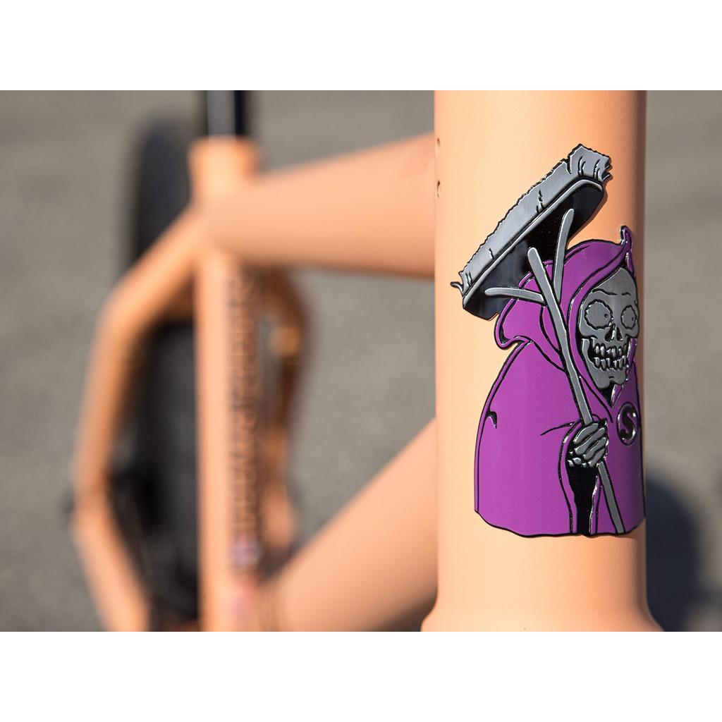 Close-up of the peach-colored Sunday Street Sweeper 20 Inch Bike frame, featuring a sticker of a grim reaper in a purple cloak with a scythe—design inspired by Jake Seeley.