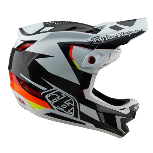 The TLD 25.1 D4 Carbon Helmet (MIPS) in Optic Black features a bold geometric black, white, and red design with "Troy Lee Designs" text and a red circular side vent—ideal for road warriors and downhill BMX enthusiasts.