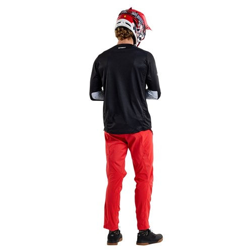 A person wearing a Troy Lee Designs motocross helmet, the TLD 25.1 Sprint Jersey in Mono Black, and red pants stands facing away from the camera.