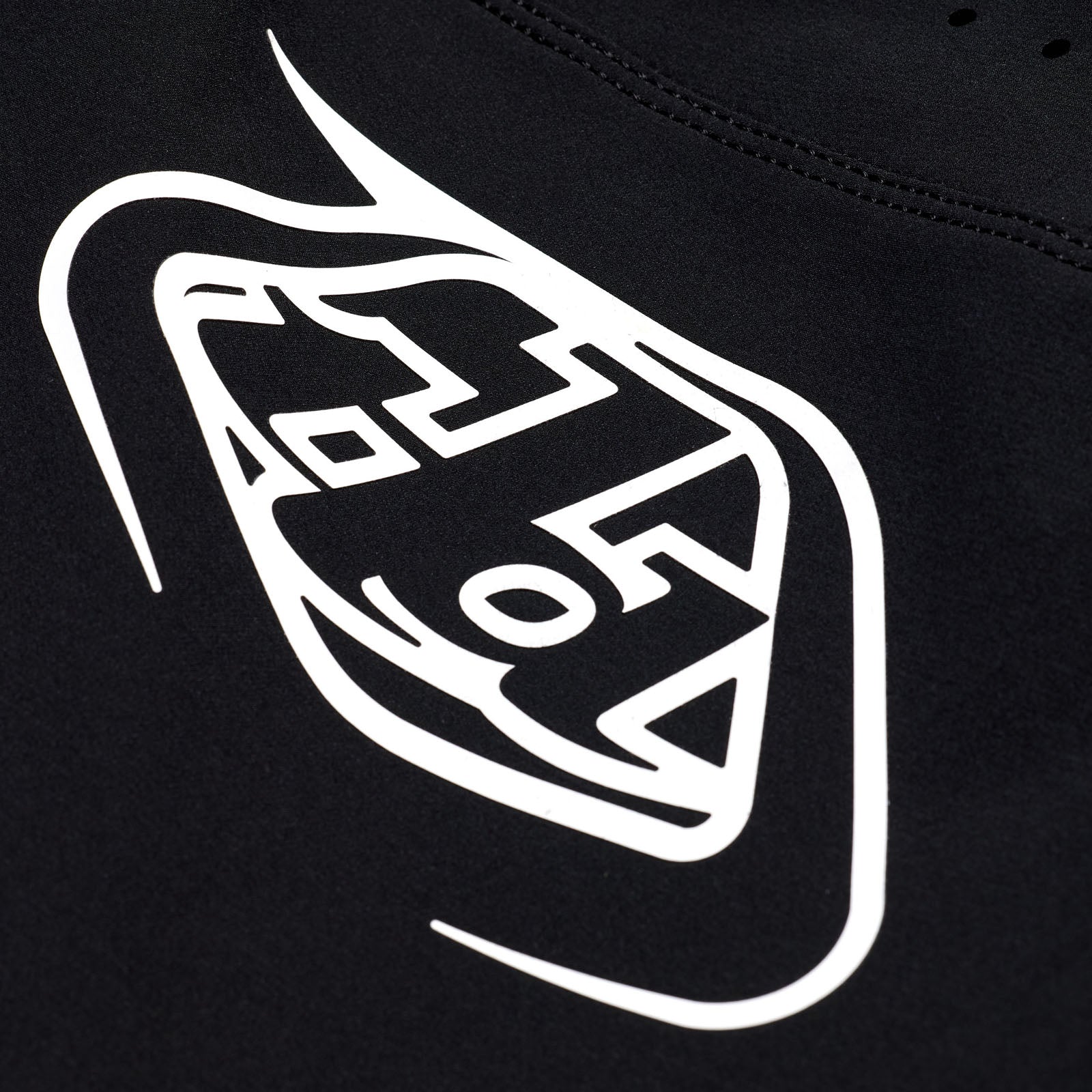 Close-up of the TLD 25.1 Sprint Pant / Mono Black fabric showcases a white geometric logo with stylized symbols and letters, reminiscent of iconic Troy Lee race pant designs.