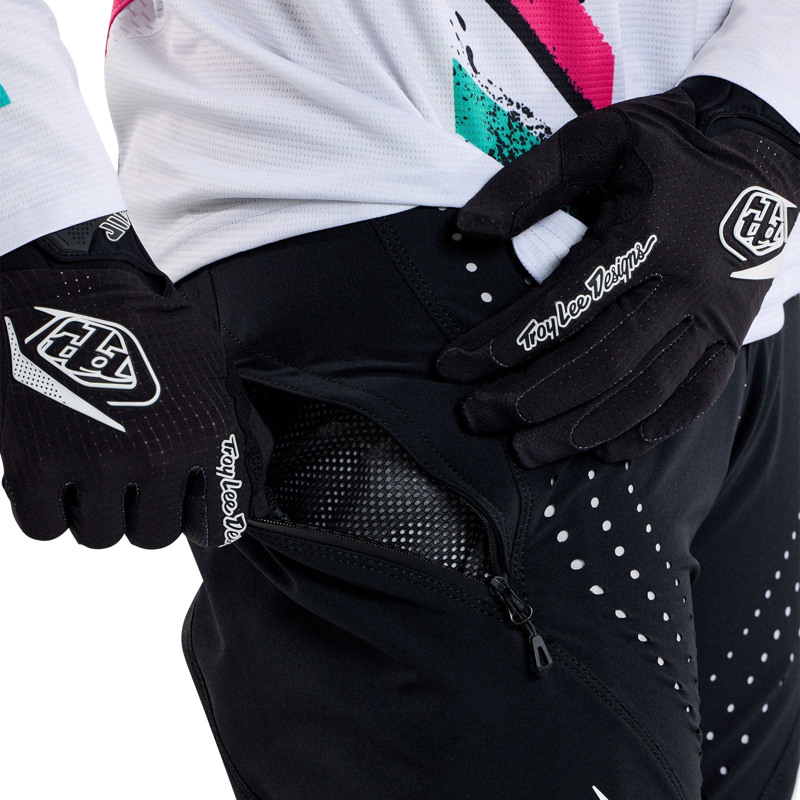 Wearing TLD 25.1 Sprint Pant in Mono Black, an individual in black gloves and athletic gear opens a zippered pocket on the sleek pants.