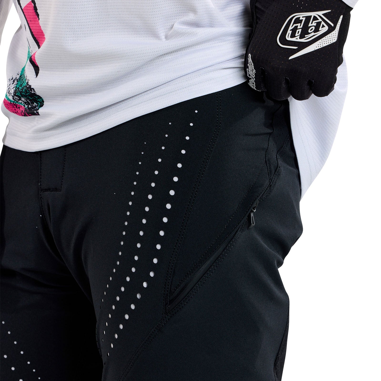 A person wearing TLD 25.1 Sprint Pant in Mono Black with a white dotted pattern, paired with a white jersey and black gloves showcasing the Troy Lee logo, slightly pulling up the jersey.