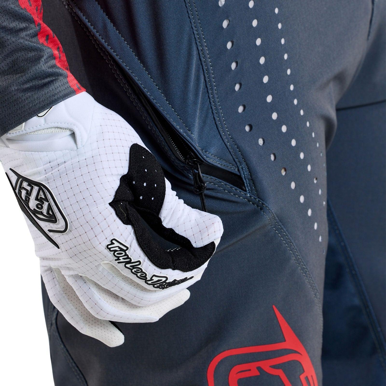 A person wearing a glove is zipping up the TLD 25.1 Sprint Pant / Mono Steel Blue, feeling race ready with its sporty design and red accents.