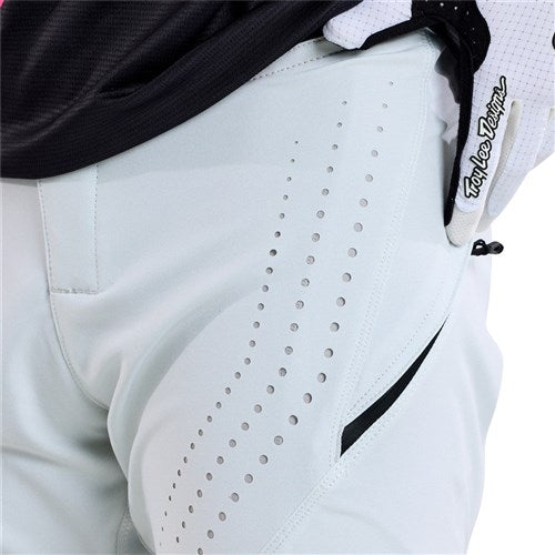 Close-up of TLD 25.1 Sprint Pant (Youth) / Chalk, featuring a light color, perforated design, and black zipper. Crafted from durable materials for resilience, a gloved hand partly appears at the top right, suggesting the sprint kit's high-performance purpose.