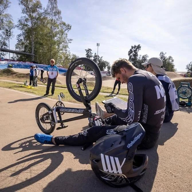 A man is sitting on the ground with a TLD D4 AS Carbon W/MIPS helmet and a bike in front of him.