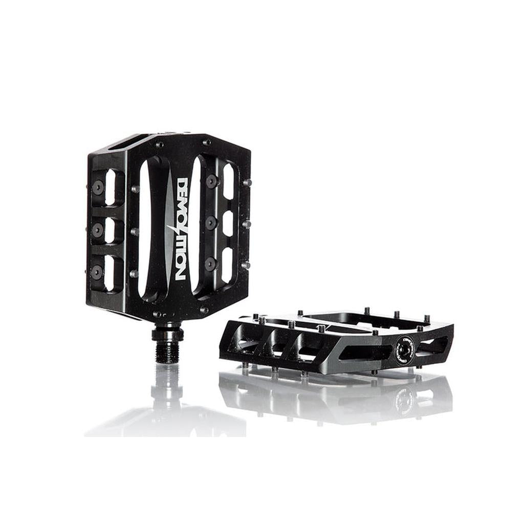 Two black Demolition Trooper Aluminum Sealed Pedals feature durable alloy bodies, visible pins for grip, and a concave feel. "Demolition" branding appears on the side, shown from both side and top views against a white background.