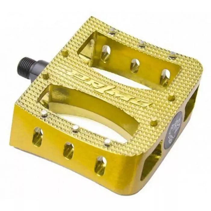 A gold, flat Primo Super Tenderizer Alloy Pedal featuring an aluminum body with a textured grip surface, multiple cutouts, and metal studs for traction. The alloy pedal displays the brand name “Primo” engraved on the top.