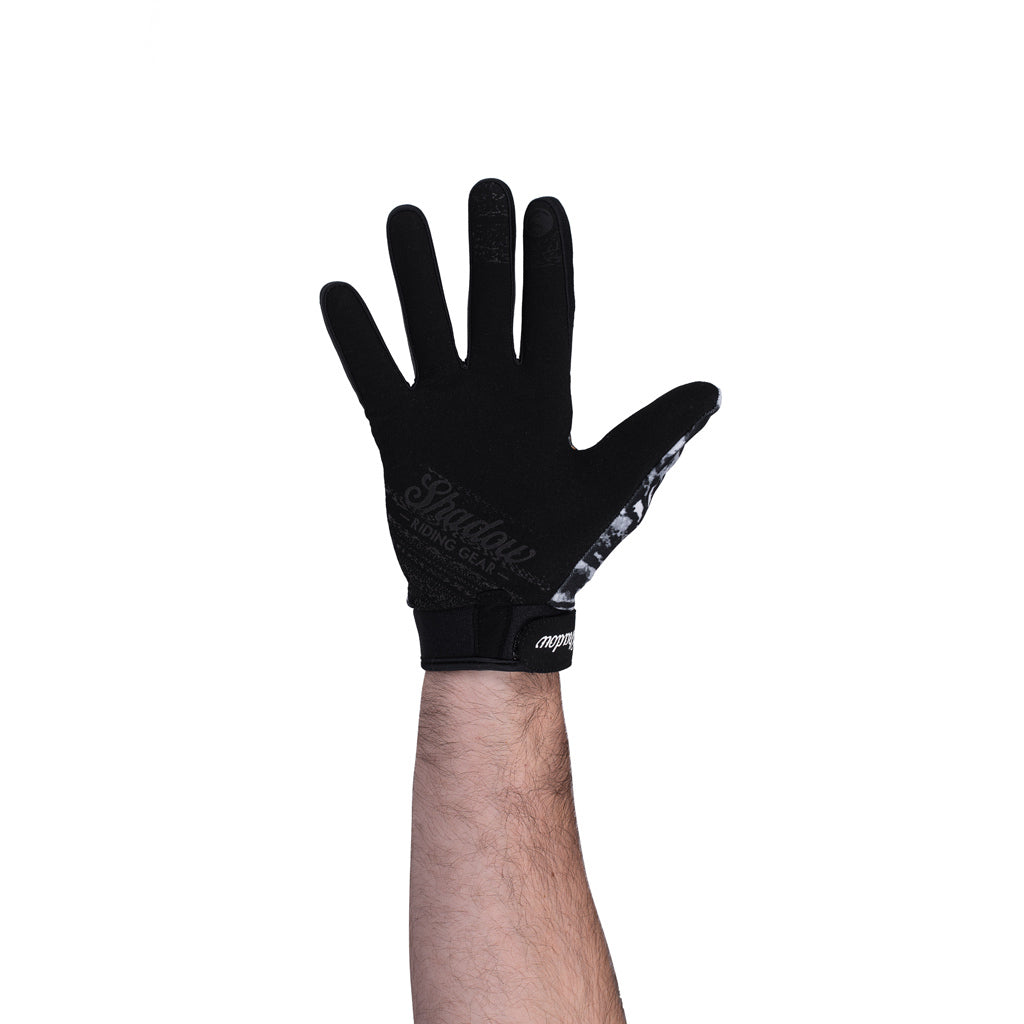 A man is holding his hand up in a Shadow Conspire Gloves / Tangerine Tye gesture in front of a white background.