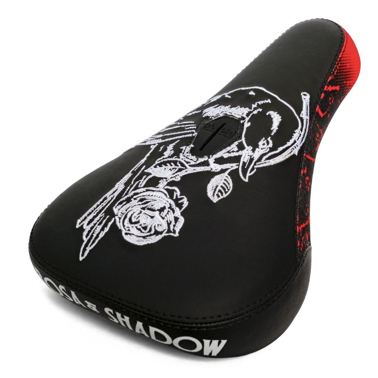 The Subrosa x Shadow Rose Crow Pivotal Seat is a black bicycle seat with white bird and rose embroidery, red rear accents, "SHADOW" side branding, and is a collaboration between Shadow and Subrosa.