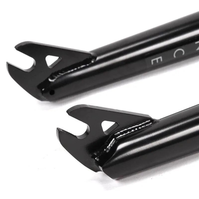 Close-up of two black heat-treated chromoly Primo Balance Fork dropouts with open slots and triangular cutouts on a white background, designed for a street fork with a 25mm offset.