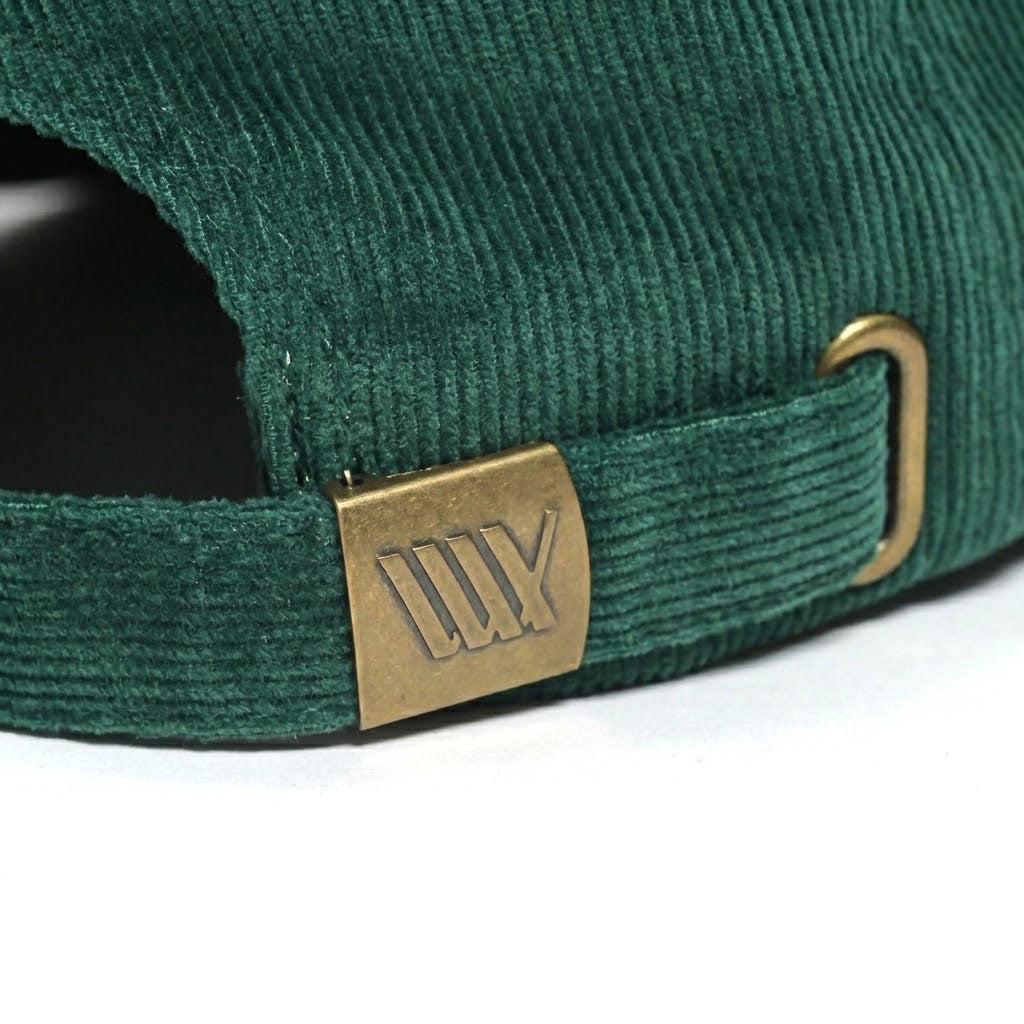 Close-up of the back strap on the LUXBMX Outfield Cap Bottle Green, featuring green corduroy fabric and a brass clasp with an engraved logo, highlighting its premium details.