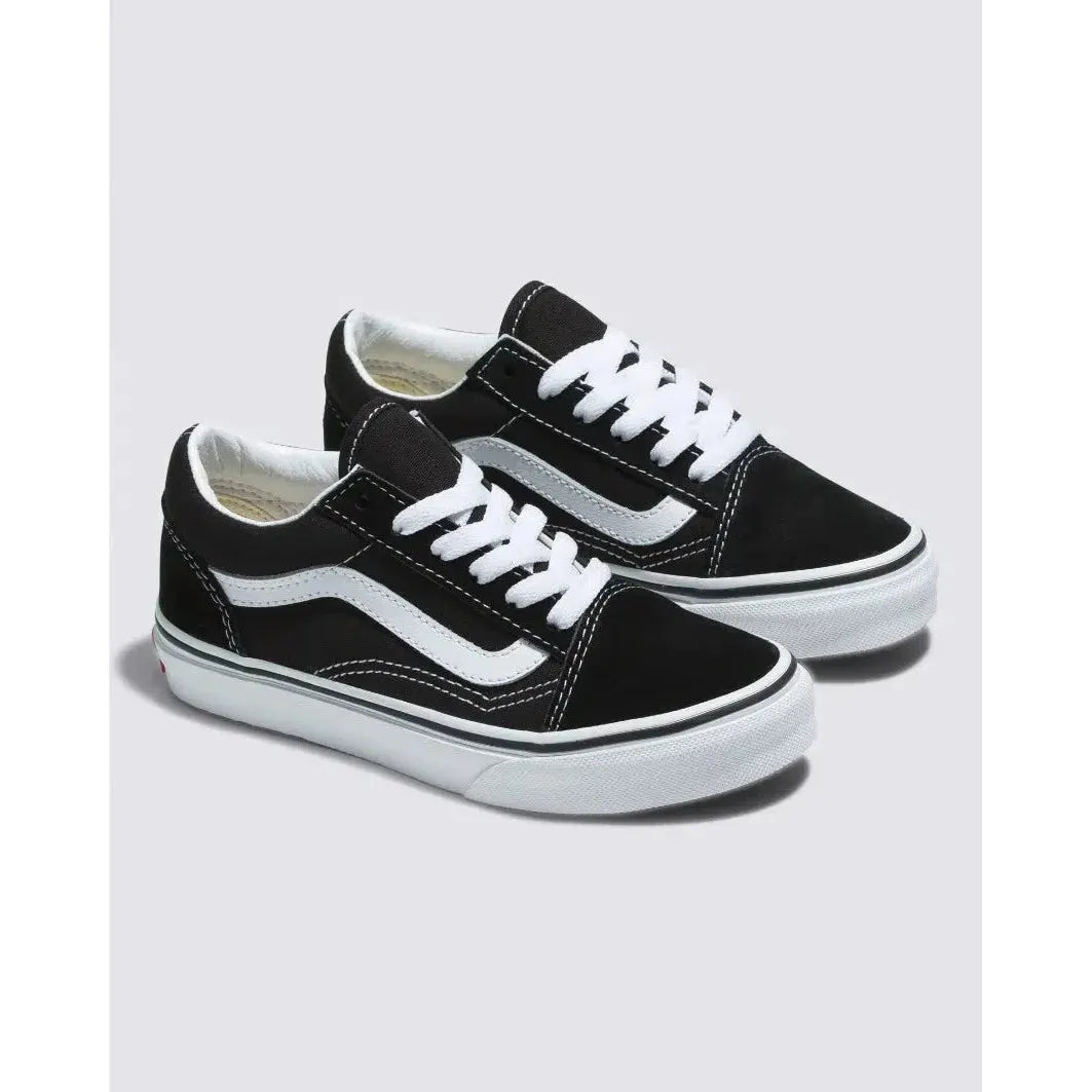 A pair of Vans Kids Old Skool Black/White low-top sneakers, featuring white laces and the signature wavy stripe, displayed on a plain light gray background.