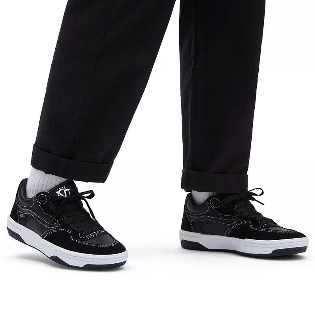 A man wearing Vans Rowan 2 Shoes - Black/White sneakers and white pants, showcasing the impact protection of the Rowan 2 skateboarding shoes.
