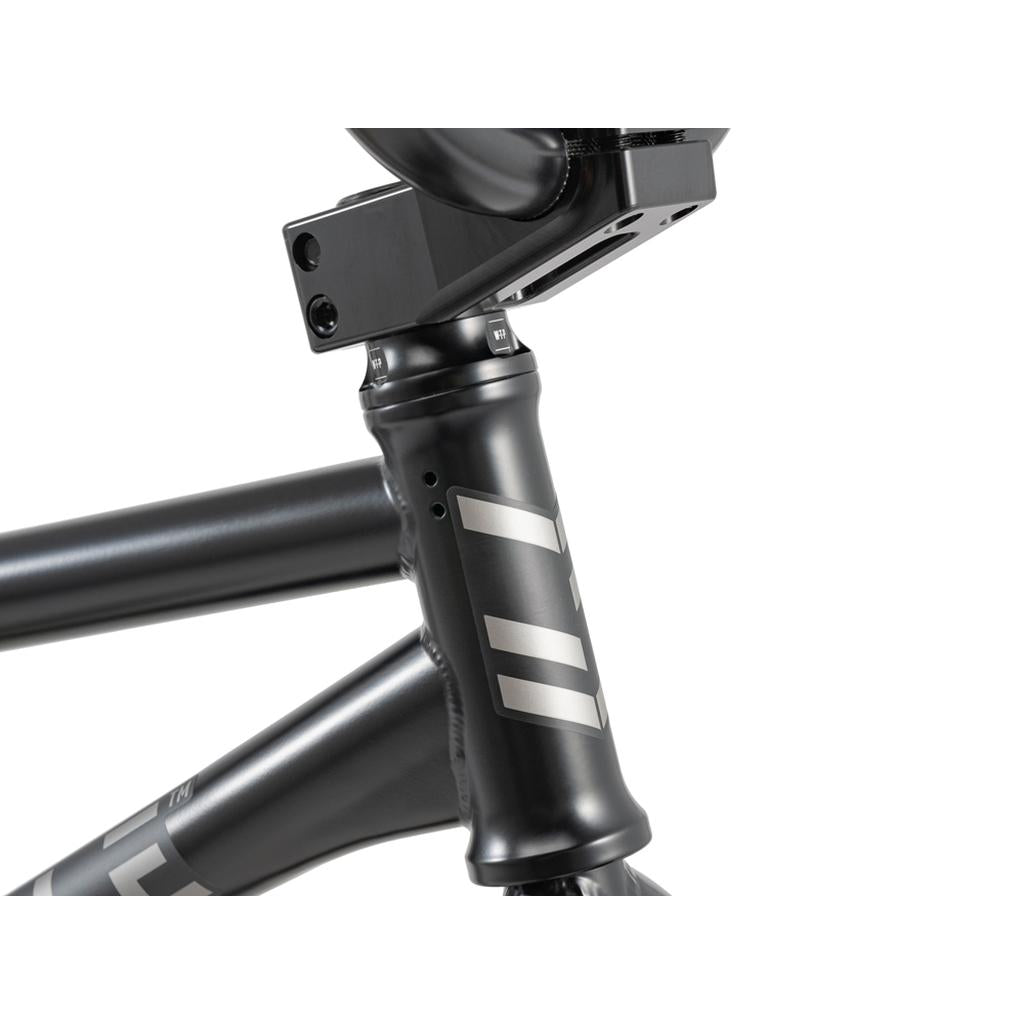 Close-up of the Wethepeople 20 inch Envy Carbonic LTD Bike’s matte black frame, featuring the head tube, top tube, part of the handlebar stem, and silver geometric decals.